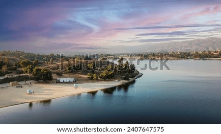 an aerial shot of a beautiful summer landscape at Puddingstone Lake with lush green trees and plants reflecting off the water, majestic mountain ranges with homes at sunset in San Dimas California USA Royalty-Free Stock Photo #2407647575