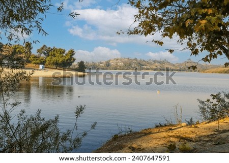 a beautiful summer landscape at Puddingstone Lake with a sandy beach, a lifeguard tower, lush green trees, rippling water, blue sky and clouds at sunset in San Dimas California USA Royalty-Free Stock Photo #2407647591