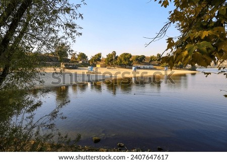a beautiful summer landscape at Puddingstone Lake with a sandy beach, a lifeguard tower, lush green trees, rippling water, blue sky and clouds at sunset in San Dimas California USA Royalty-Free Stock Photo #2407647617