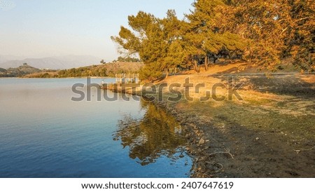 an aerial shot of a beautiful summer landscape at Puddingstone Lake with lush green trees and plants reflecting off the water, majestic mountain ranges with homes at sunset in San Dimas California USA Royalty-Free Stock Photo #2407647619