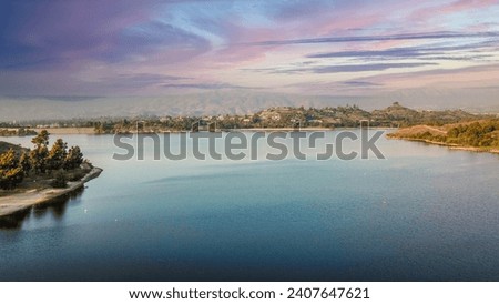 an aerial shot of a beautiful summer landscape at Puddingstone Lake with lush green trees and plants reflecting off the water, majestic mountain ranges with homes at sunset in San Dimas California USA Royalty-Free Stock Photo #2407647621