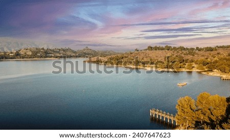 an aerial shot of a beautiful summer landscape at Puddingstone Lake with lush green trees and plants reflecting off the water, majestic mountain ranges with homes at sunset in San Dimas California USA Royalty-Free Stock Photo #2407647623