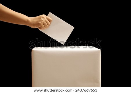 hand holding the ballot into the ballot box. election day concept isolated black background.