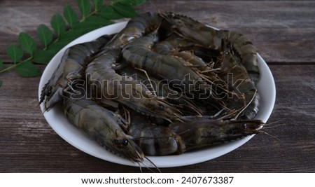 A group of Big Fresh vanammei shrimp or prawn in white ceramic dish with curry leaves at wooden table. Tiger Prawn. Vaname. Litopenaeus vannamei. Seafood. Protein. Udang Windu. Japanese Food. Royalty-Free Stock Photo #2407673387