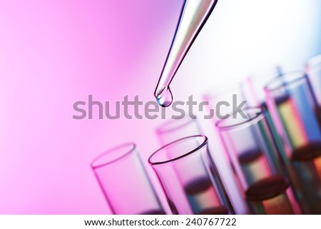 Pipette adding liquid to the one of test-tubes on the pink shining background