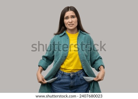 Upset poor woman showing empty pockets and looking frustrated about loans and debts, has no money, jobless going bankrupt, wearing casual style jacket. Indoor studio shot isolated on gray background. Royalty-Free Stock Photo #2407680023