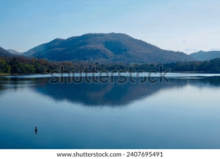 A wide river with mountains, trees and a beautiful sky. There was a shadow of a mountain on the surface of the water. It is a very beautiful picture of nature.