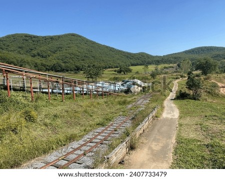 a photography of a train traveling down tracks next to a lush green hillside.