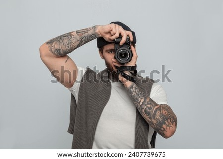 Handsome man professional with tattoo with knitted hat with knitted sweater holding mirrorless photo camera and taking photos in studio