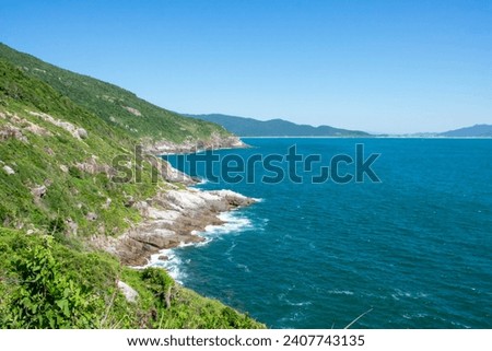 The picture shows a rocky coastline with turquoise-green water, green slopes and an absolutely blue sky without clouds.