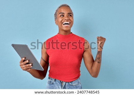 Young overjoyed cute African American woman freelancer with tablet computer makes victory hand wave after successfully completing project or new career achievement stands on turquoise background.