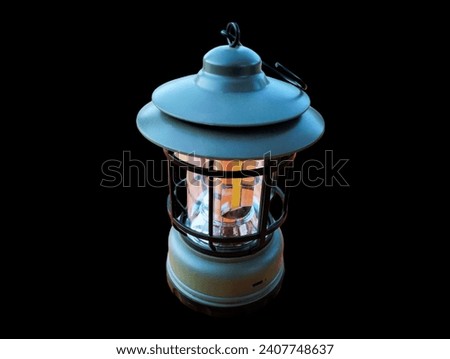 The black background in the picture is a lighted lantern with a turquoise holder, a black steel frame, and a fire starter. It uses oil to start a fire. It is a fire starter, used in times of emergency