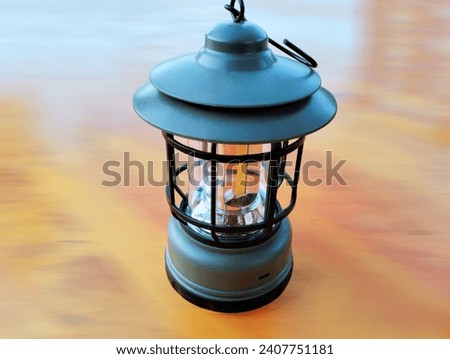 The  background in the picture is a lighted lantern with a turquoise holder, a black steel frame, and a fire starter. It uses oil to start a fire. It is a fire starter, used in times of emergency