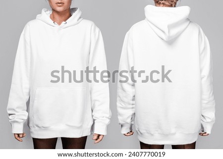 Front and back views of a woman wearing a white, oversized hoodie with blank space, ideal for a mockup, set against gray background. Royalty-Free Stock Photo #2407770019