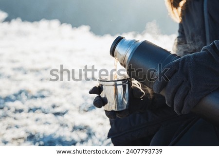 Hot tea poured from a thermos into a mug, cold winter, warm up with warm drinks, hiking in the mountains in winter, dishes for boiling water. High quality photo