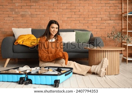 Young woman packing winter clothes in suitcase at home Royalty-Free Stock Photo #2407794353