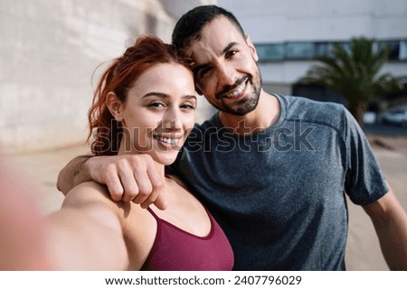 Young fit couple taking selfie smiling after training running outside. Sports lovely joyful active fitness friends standing taking a picture outdoors.