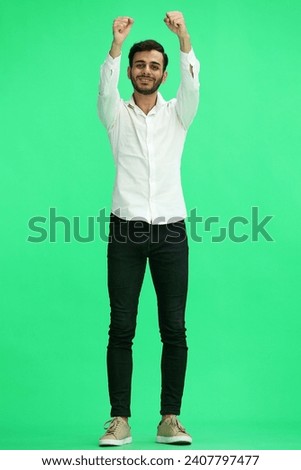A young man on a green background in full growth raised his hands in the air