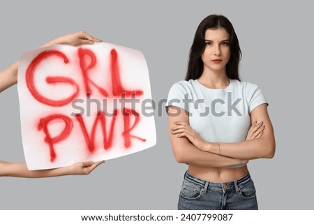 Young woman with crossed arms and sign GRL PWR on grey background. Feminism concept