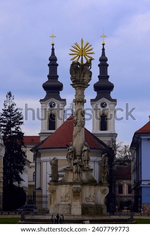 Urban image from Timisoara, Romania. The Plague Statue or Holy Trinity Statue is framed by the towers of the Serbian Church. Royalty-Free Stock Photo #2407799773
