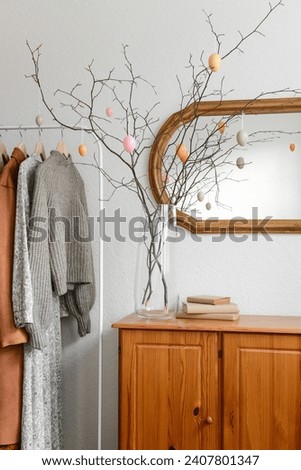 Vase with tree branches and hanging Easter eggs on cabinet in interior of hallway