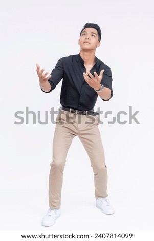 A worried young asian man anticipating to catch something or someone falling down, extending his hands to the left. Full body photo, isolated on a white background. Royalty-Free Stock Photo #2407814099