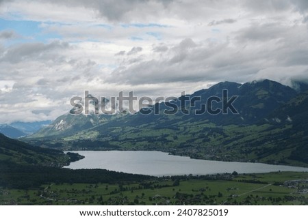 The aerial perspective showcases the grandeur of a Swiss lake nestled within a vast mountain range, under a canopy of clouds.