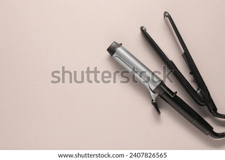 Curling iron and hair straightener on beige background, top view. Space for text Royalty-Free Stock Photo #2407826565