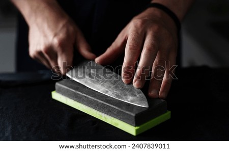 Man Sharpening Kitchen Knife With A Whetstone Stands Out Against Black Background