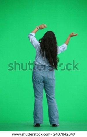 A girl in a blue shirt, on a green background, in full height, waving her arms, back view Royalty-Free Stock Photo #2407842849