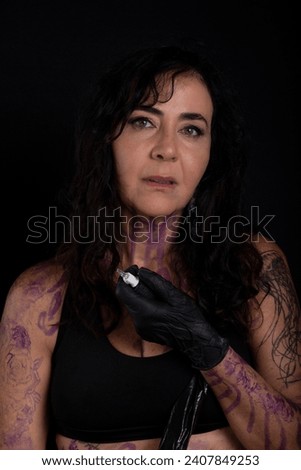 Beautiful artist holding tattoo machine looking at camera against black background