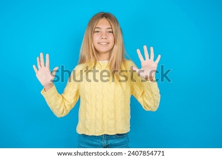 Beautiful kid girl wearing yellow sweater holding notebook showing and pointing up with fingers number ten while smiling confident and happy.