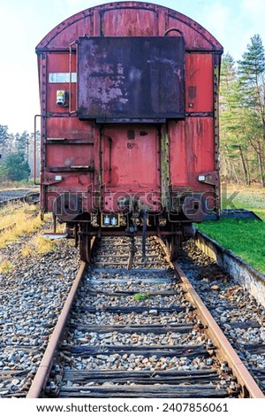 Front view of a rusty red metal freight car on disused train tracks at old station, coupling stops, trees in background, sunny autumn day with blue sky in As, Limburg Belgium Royalty-Free Stock Photo #2407856061
