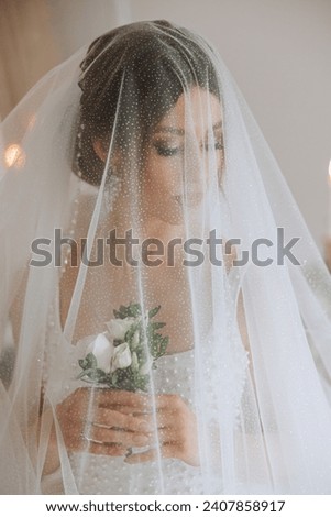 A luxurious bride with a beautiful hairstyle and a gorgeous dress is getting ready for the wedding ceremony in the morning. Morning photo of the bride at home or in a hotel room. Professional makeup.