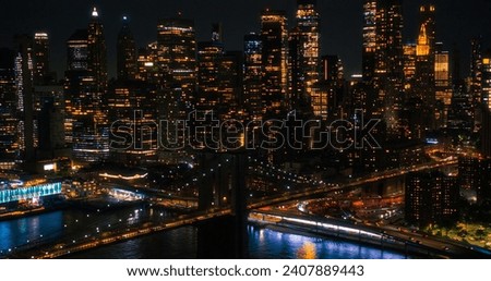 Aerial Helicopter Cinematic Night Scene with Top Down View of the Brooklyn Bridge Switching to a Panoramic Shot with Skyscrapers Cityscape. Beautiful Office Buildings with Lights in the Dark