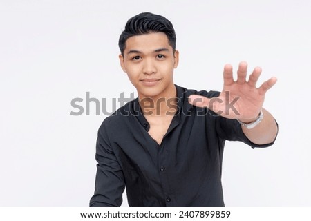 A young asian man puts his hand forward, diffusing a tense situation. Assuring someone everything will be fine.. Wearing black polo shirt, isolated on a white background.