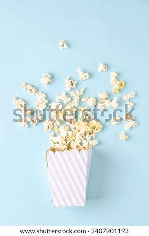 A striped bucket of popcorn on light blue background, top view and copy space. Vertical format.