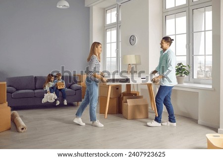 Happy smiling family couple with two kids boy and girl on background arranging furniture in a new apartment on moving day with unpacked boxes. Relocating, real estate, mortgage concept. Royalty-Free Stock Photo #2407923625