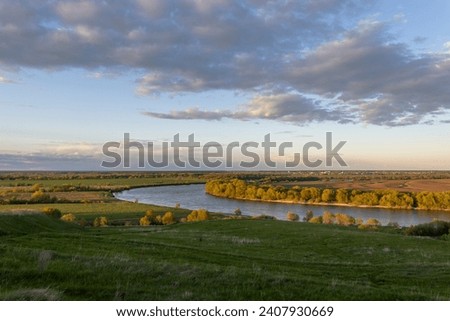 A calming evening landscape over expanses of water meadows, green grass and a sunset sky with clouds above the horizon