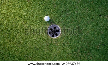 Selective focus. white golf ball in hole on green grass good for background with sunlight. golf ball beside the golf hole.                                Royalty-Free Stock Photo #2407937689