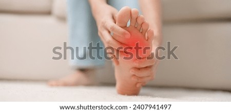 woman having barefoot pain during sitting on couch at home. Foot ache due to Plantar fasciitis and waking longtime. Health and medical concept Royalty-Free Stock Photo #2407941497