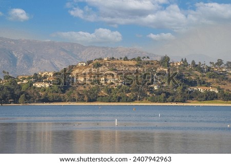 a gorgeous shot of the vast still lake waters with majestic mountain ranges covered with homes and lush green and autumn colored trees at Puddingstone Lake in San Dimas California USA	 Royalty-Free Stock Photo #2407942963