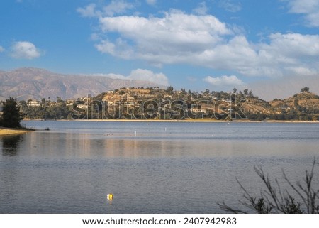 a gorgeous shot of the vast still lake waters with majestic mountain ranges covered with homes and lush green and autumn colored trees at Puddingstone Lake in San Dimas California USA	 Royalty-Free Stock Photo #2407942983