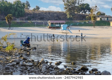 a man sitting in a chair fishing on the lake with lush green trees and plants in a beautiful summer landscape at Puddingstone Lake in San Dimas California USA Royalty-Free Stock Photo #2407942985