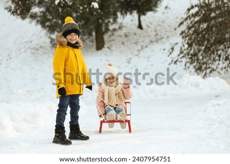 Little boy pulling sledge with his sister through snow in winter park