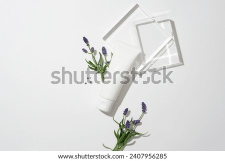 An unlabeled cosmetic tube decorated with lavender flowers and two glass platforms. White background for text design. Essential oils made from lavender flowers and leaves help heal wounds. Royalty-Free Stock Photo #2407956285