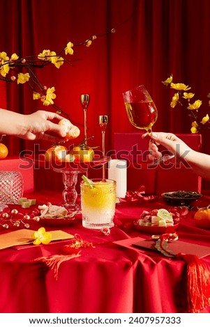Front view of Tet holiday party table with bright red background. Scene with decorations, yellow apricot flowers, jam, wine, tangerines, red envelopes and gift boxes. Advertising. Royalty-Free Stock Photo #2407957333