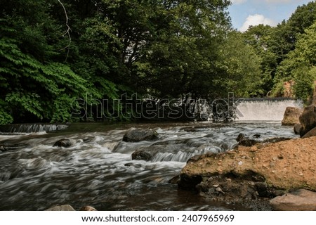 A river and waterfall meandering through Burrs Country Park in Bury, England. Royalty-Free Stock Photo #2407965969