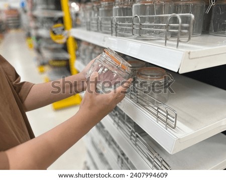 Young Woman With Shopping, woman hand holds jar of sauce on blurred background, row of shelves with groceries in supermarket, concept of marketing, prices for consumer goods, consumer basket