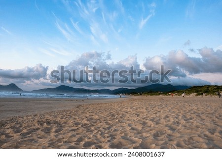 The picture shows the sandy beach of Campeche on Santa Catarina Island in the early hours of the morning. The green wooded slopes of the island's mountains can be seen in the background.